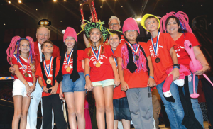 Pictured (l-r, front) are students Sofia Vinueza, Lorenzo Vinueza, Leah Melendez, Kennedy Todd, Andres Laventman, Alex Eum and Matthew Lamas, with coach/parent Lida Mari-Todd; (back) Odyssey of the Mind founder Dr. Sam Micklus (left) and coach/parent Milton Todd holding the trophy. (Photo courtesy of Odyssey of the Mind.)